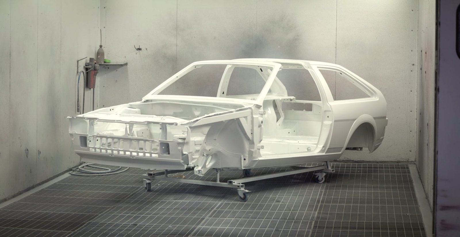 A bare car body in white primer on a dolly inside a paint booth