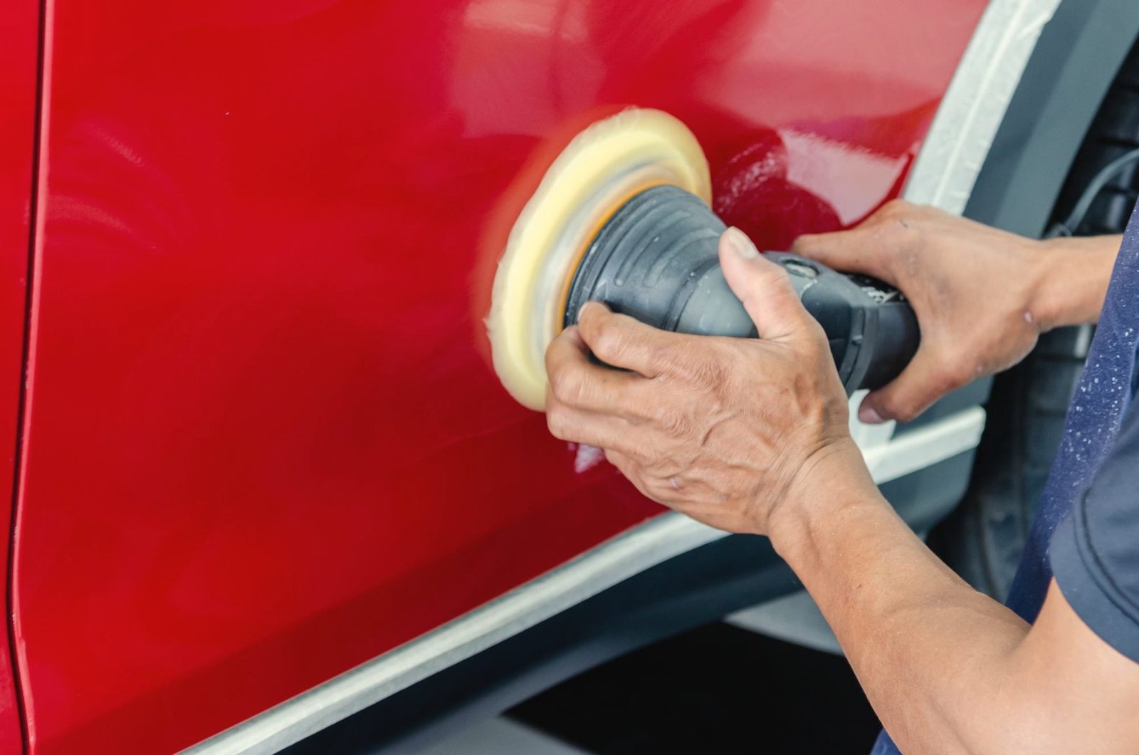 Hands running a foam buffing pad across a glossy red door
