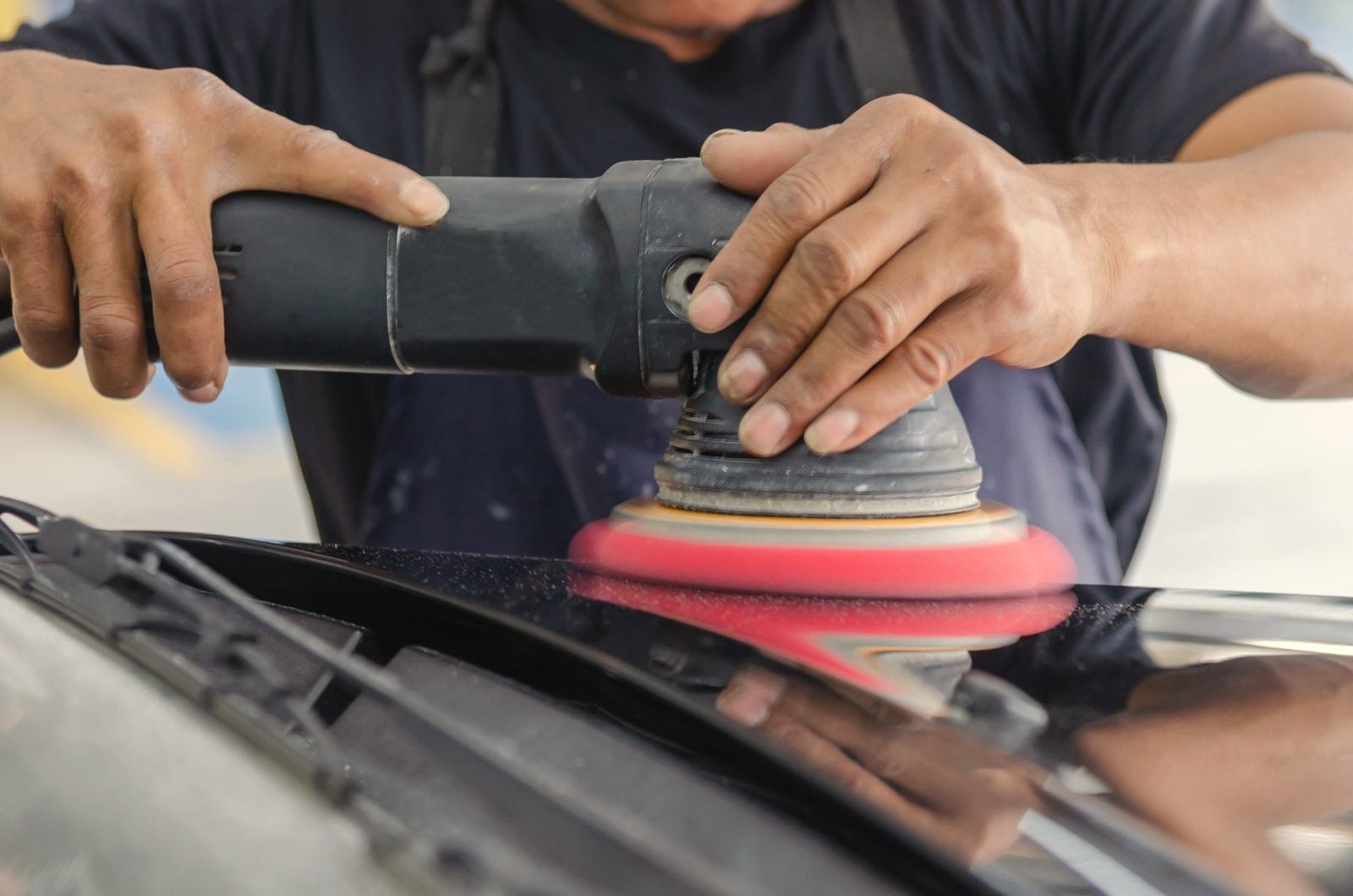 A polisher with a red pad working across a black hood